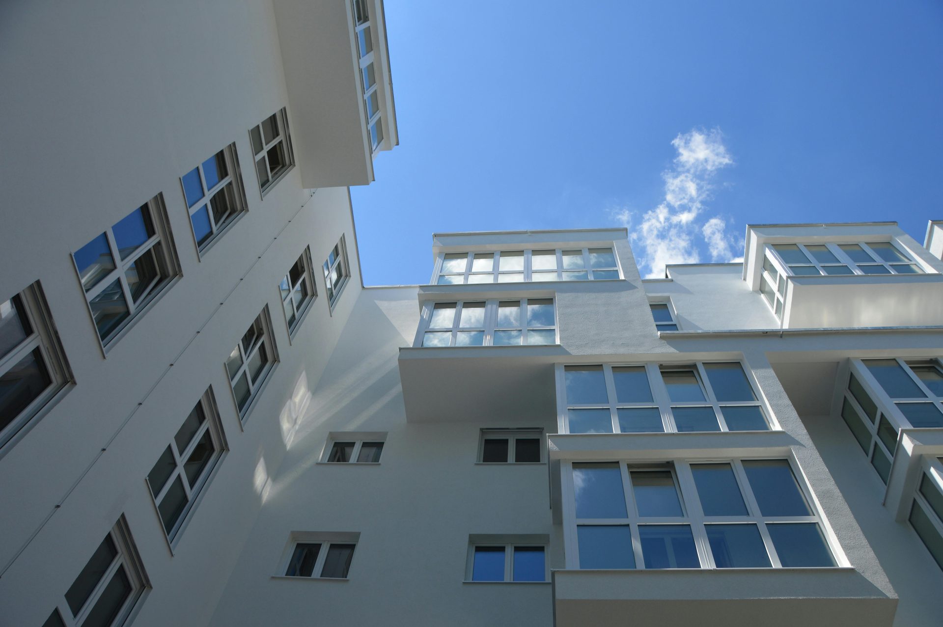 Ansicht von unten auf ein modernes, weißes Gebäude vor klarem, blauem Himmel, das zeitgenössische Architektur präsentiert.
