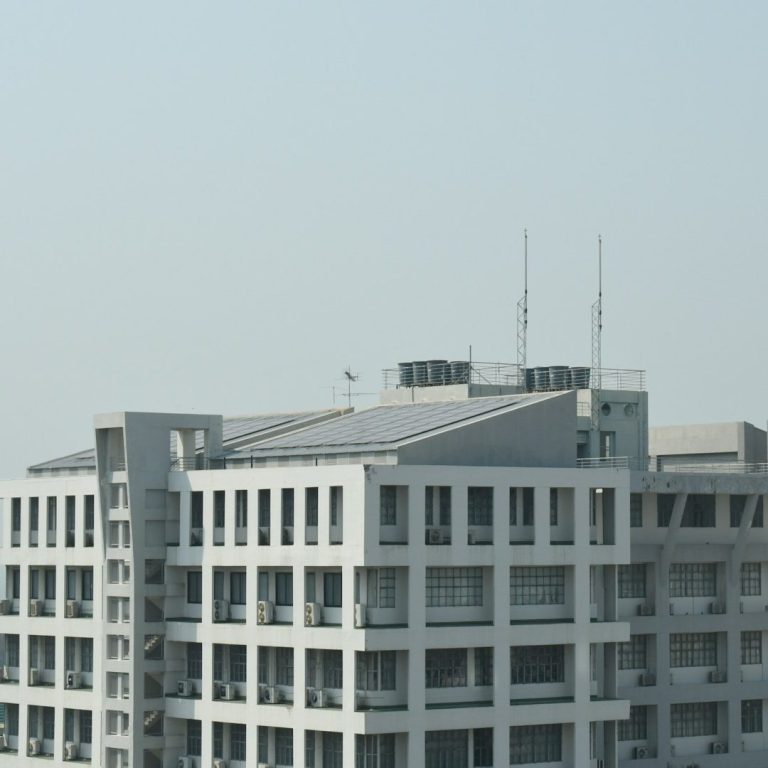Verwaltung Graues Bürogebäude mit Solarpanelen und Antennen auf dem Dach.